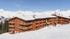 A wooden chalet with multiple balconies, set against a backdrop of snow-covered mountains.