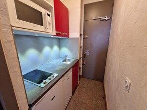 Eine kompakte Küche mit Mikrowelle, Spüle und roten Schränken.