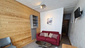A living room with a red sofa, a grey armchair, a wooden coffee table, and a TV mounted on the wall. - 10m from ski slopes, view ski slopes, balcony, tv, ski locker, 25m², La Plagne (La Plagne)