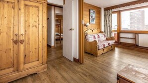 A room with wooden flooring, a bed with patterned bedding, a wooden wardrobe, and a window with a view of buildings. - 20m from ski slopes, 5th floor, balcony, tv, ski locker, 50m², La Plagne (La Plagne)