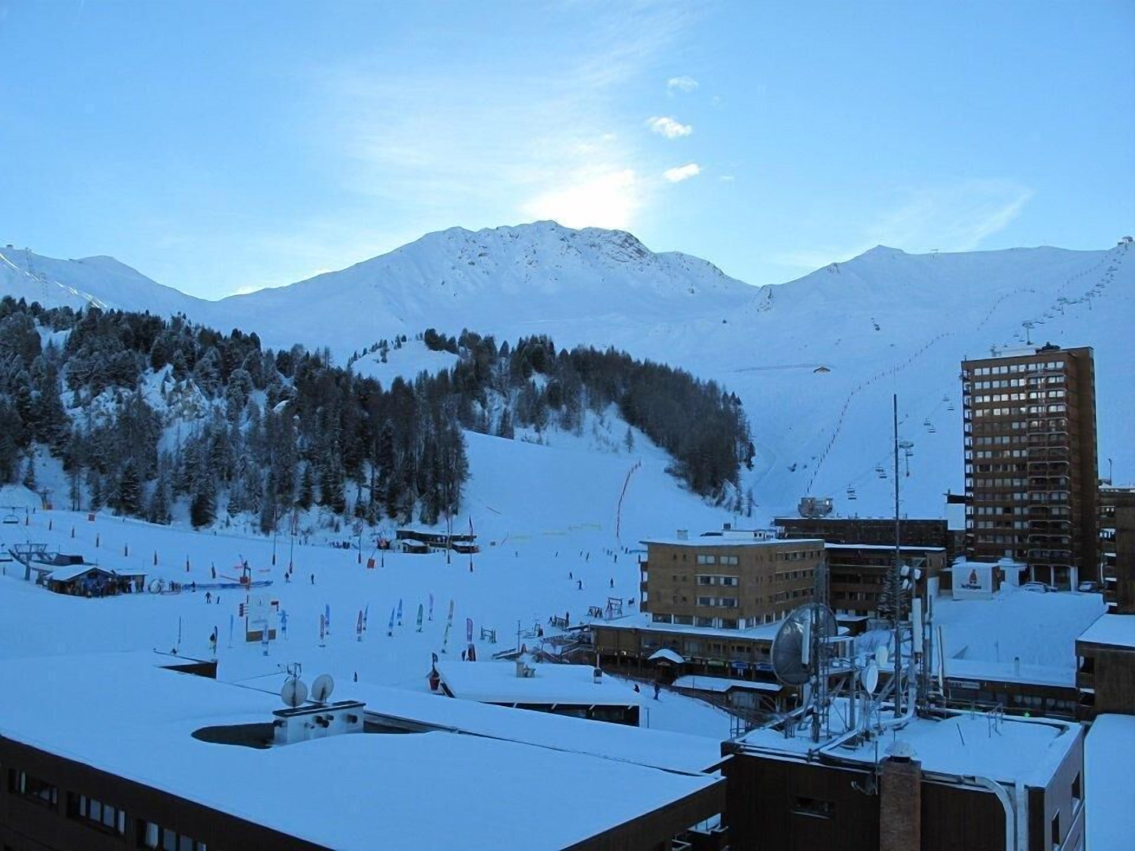 A snow-covered mountain with a ski resort in the foreground, featuring buildings and ski lifts.