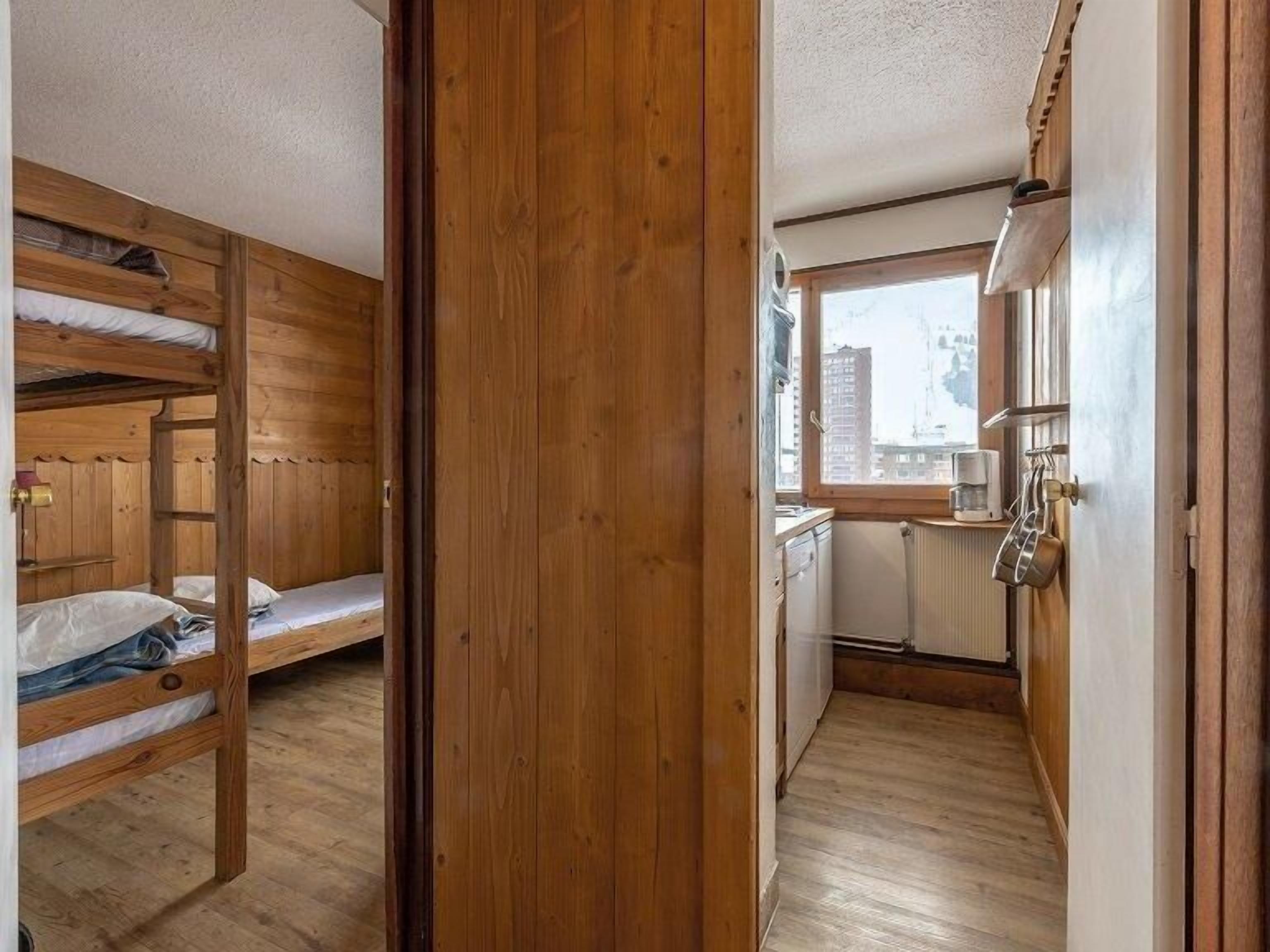 Habitación compacta con literas, un pequeño kitchenette y una ventana con vistas a edificios.