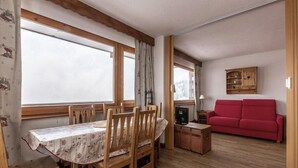 A dining area with a wooden table and chairs, a red sofa, and a cabinet. - 20m from ski slopes, 5th floor, balcony, tv, ski locker, 50m², La Plagne (La Plagne)