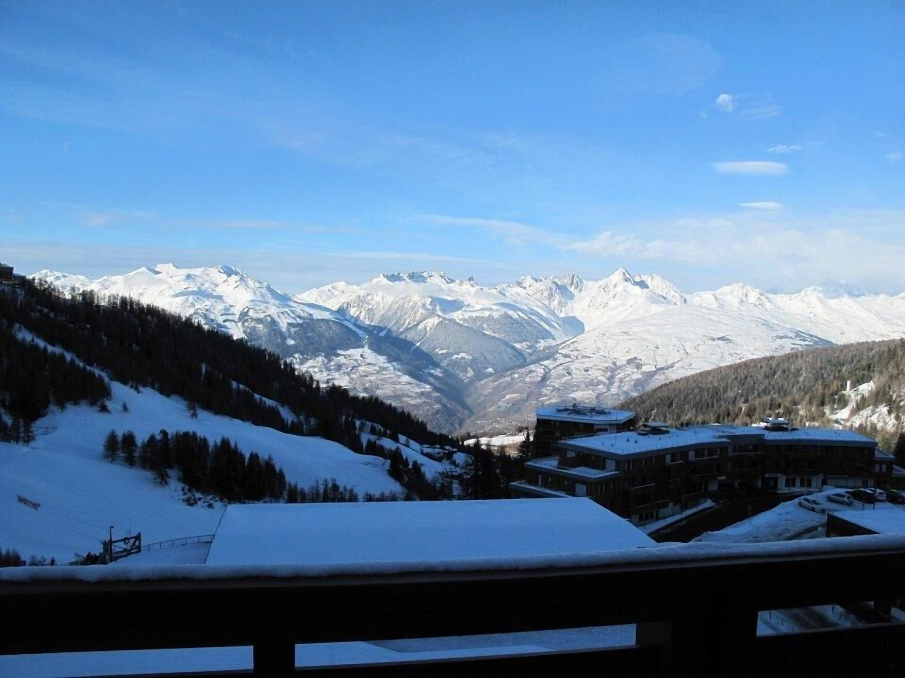 A snow-covered mountain landscape with a building featuring a flat roof and multiple windows, likely a hotel or lodge, in the foreground.