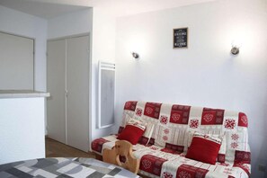 A room with a bed, a wooden chair, a white door, and a wall-mounted light fixture.
