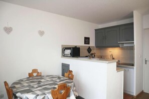 A compact kitchen with a microwave, a small sink, and a dishwasher. There is a dining table with a checkered tablecloth and wooden chairs.