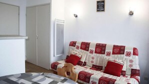 A cozy room with a bed, a wooden chair, a sofa with red and white patterned bedding, and a wall-mounted light fixture. - 15m from ski slopes, 6th floor, balcony, 23m², Les Orres (Les Orres)