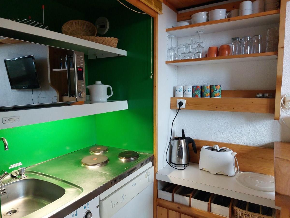 A compact kitchen with a green wall, a sink, a stove, and shelves with kitchenware.