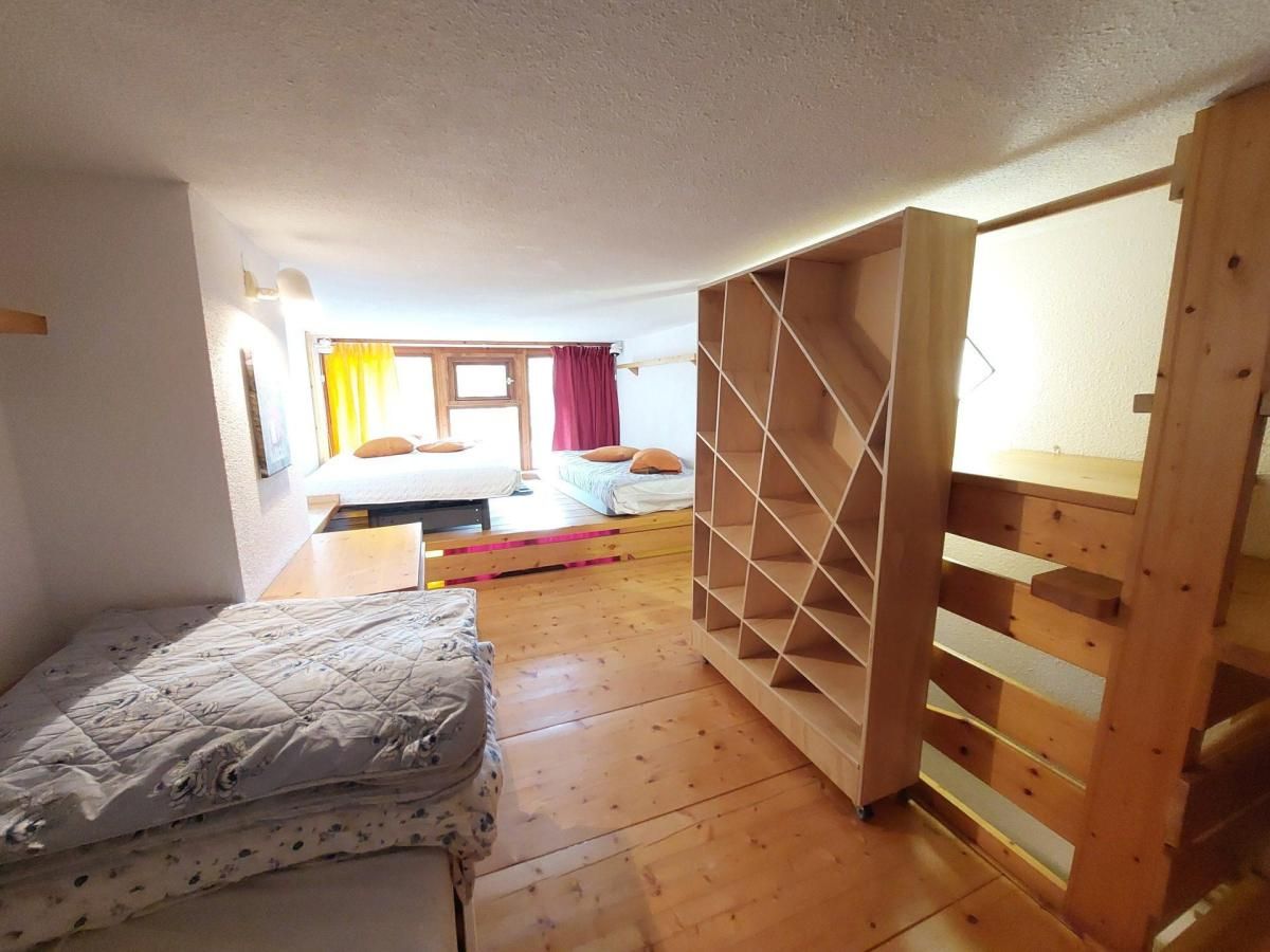 A compact room with a bed, a wooden wardrobe, and a small table.