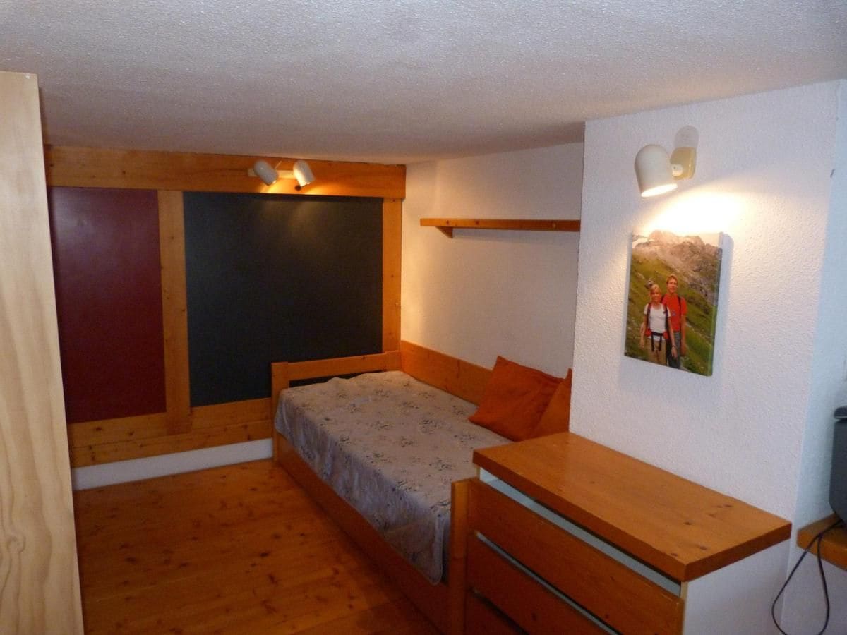 A small, cozy room with a bed, a wooden desk, and a wall-mounted shelf.