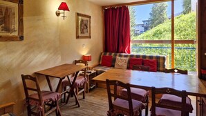 Ein gemütlicher Essbereich mit Holztisch und -stühlen, einem roten Sofa mit Kissen sowie einem großen Fenster mit Blick auf Grünflächen.