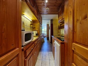 A narrow kitchen with wooden cabinets and a microwave.