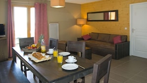 A dining area with a wooden table set for breakfast, a sofa, and a TV in the background. - 30m from resort center, swimming pool, sauna, hammam, terrace, balcony, tv, ski locker, 66m² (Font-Romeu-Odeillo-Via)