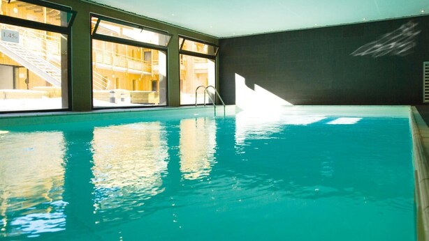 An indoor swimming pool with clear glass walls, a ladder, and a view of a wooden structure outside. - 30m from resort center, swimming pool, sauna, hammam, terrace, balcony, tv, ski locker, 66m² (Font-Romeu-Odeillo-Via)