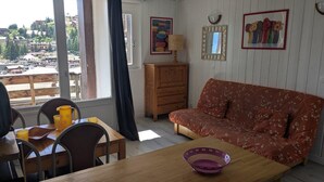 A room with a wooden dining table, a sofa, and a view of a town through large windows. - 50m from ski slopes, 2nd floor, tv, 30m², Orcières Merlette 1850 (Orcières)
