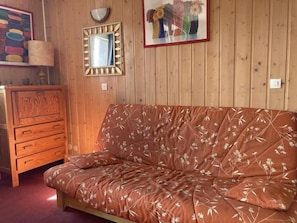 Une pièce aux murs lambrissés, avec un canapé à motifs floraux, une commode en bois, un miroir et un tableau encadré accroché au mur.