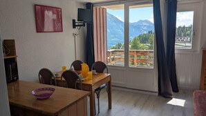A room with a wooden dining table, chairs, a TV mounted on the wall, and a large window with curtains. - 50m from ski slopes, 2nd floor, tv, 30m², Orcières Merlette 1850 (Orcières)