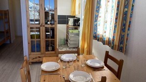 Een eethoek met een houten tafel gedekt voor vier personen, een kast met glazen deuren, en een keuken op de achtergrond.