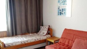 Ein kleines Zimmer mit einem Bett, einer roten Couch, einem Holzsessel und einem kleinen Tisch.