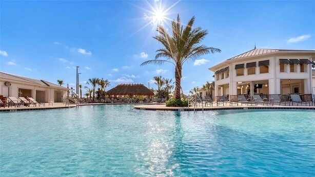 A large swimming pool with lounge chairs and palm trees, surrounded by buildings. - Great Location! Disney-Universal-Kid Gear-Free Pool Heat-Lake view- Family Fun (Kissimmee)