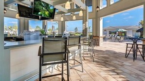 A spacious outdoor bar area with a TV screen, multiple seating arrangements, and large windows offering a view of the surroundings. - Great Location! Disney-Universal-Kid Gear-Free Pool Heat-Lake view- Family Fun (Kissimmee)