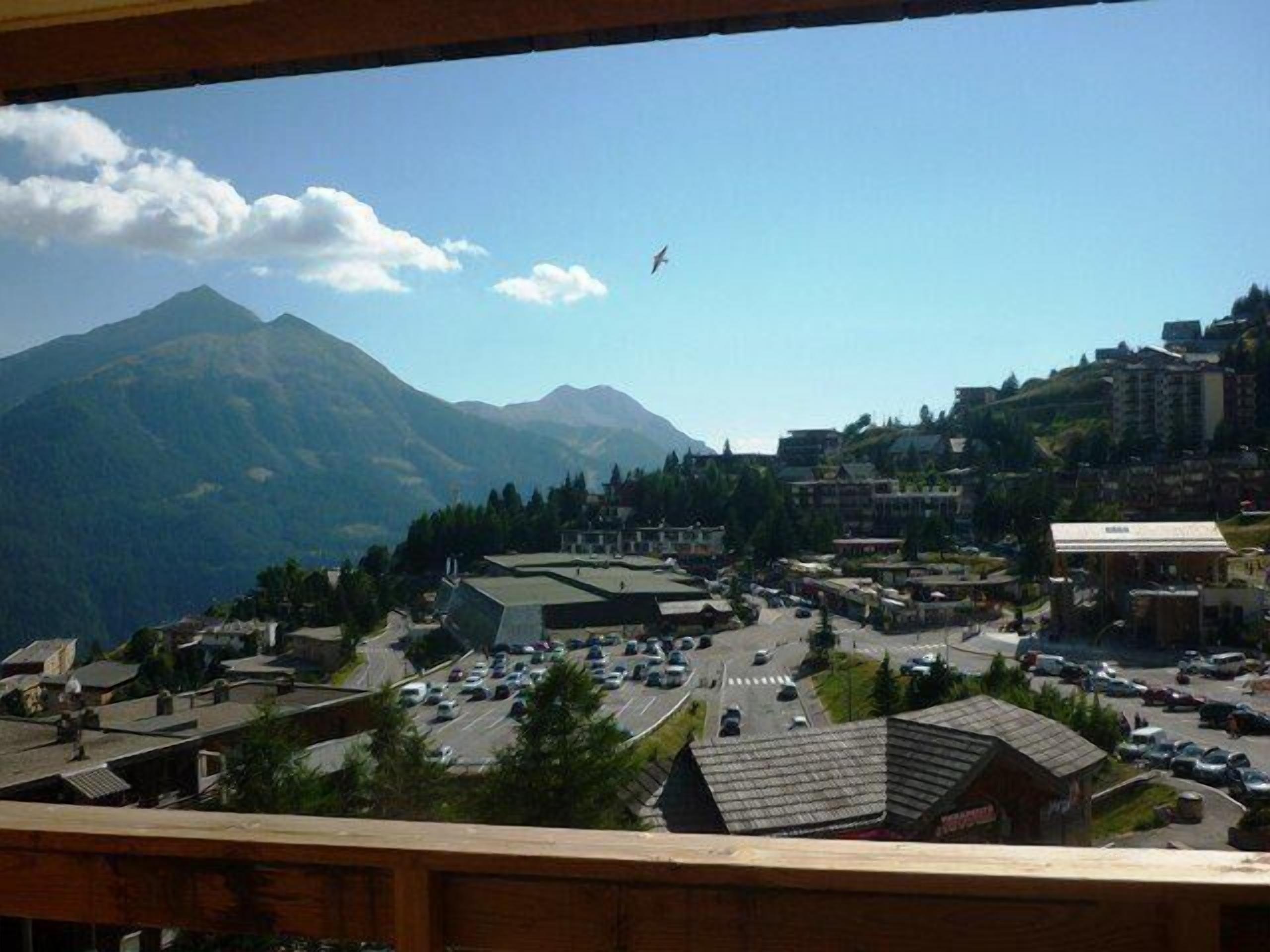 A town with a mountainous backdrop, featuring a mix of residential and commercial buildings, a central road, and a clear sky.