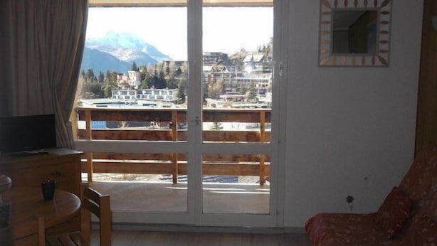 A room with a wooden floor, a dining table with chairs, a sofa, a TV, and a large window offering a mountain view. - 50m from ski slopes, 3rd floor, tv, 25m², Orcières Merlette 1850 (Orcières)