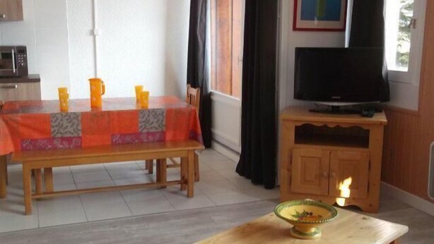 Ein Essbereich mit einem Tisch für vier Personen, einem Fernseher auf einem Holzboden und einem kleinen Tisch mit einer Schüssel.
