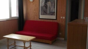 Ein Zimmer mit einer Holzwand, einem roten Sofa, einem Holztisch und einem gerahmten Kunstwerk.