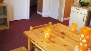 Una mesa de comedor de madera con cuatro candelabros naranjas, un banco y un armario blanco con un cajón.