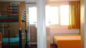 Habitación tipo dormitorio con literas, una cama individual, una ventana con cortinas y una puerta.