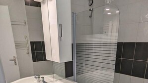 A modern bathroom with a white sink, mirror, and a glass-enclosed shower.
