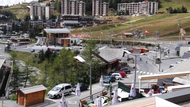 Eine Stadt mit modernen Gebäuden, einer kleinen Holzhütte und einem Parkplatz mit Autos und Sonnenschirmen.