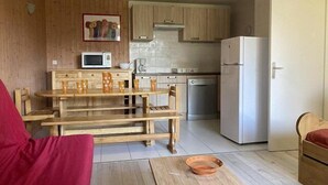A compact kitchen with wooden cabinets, a microwave, a refrigerator, and a dining area with a table and chairs. - 50m from ski slopes, 6th floor, tv, 45m², Orcières Merlette 1850 (Orcières)