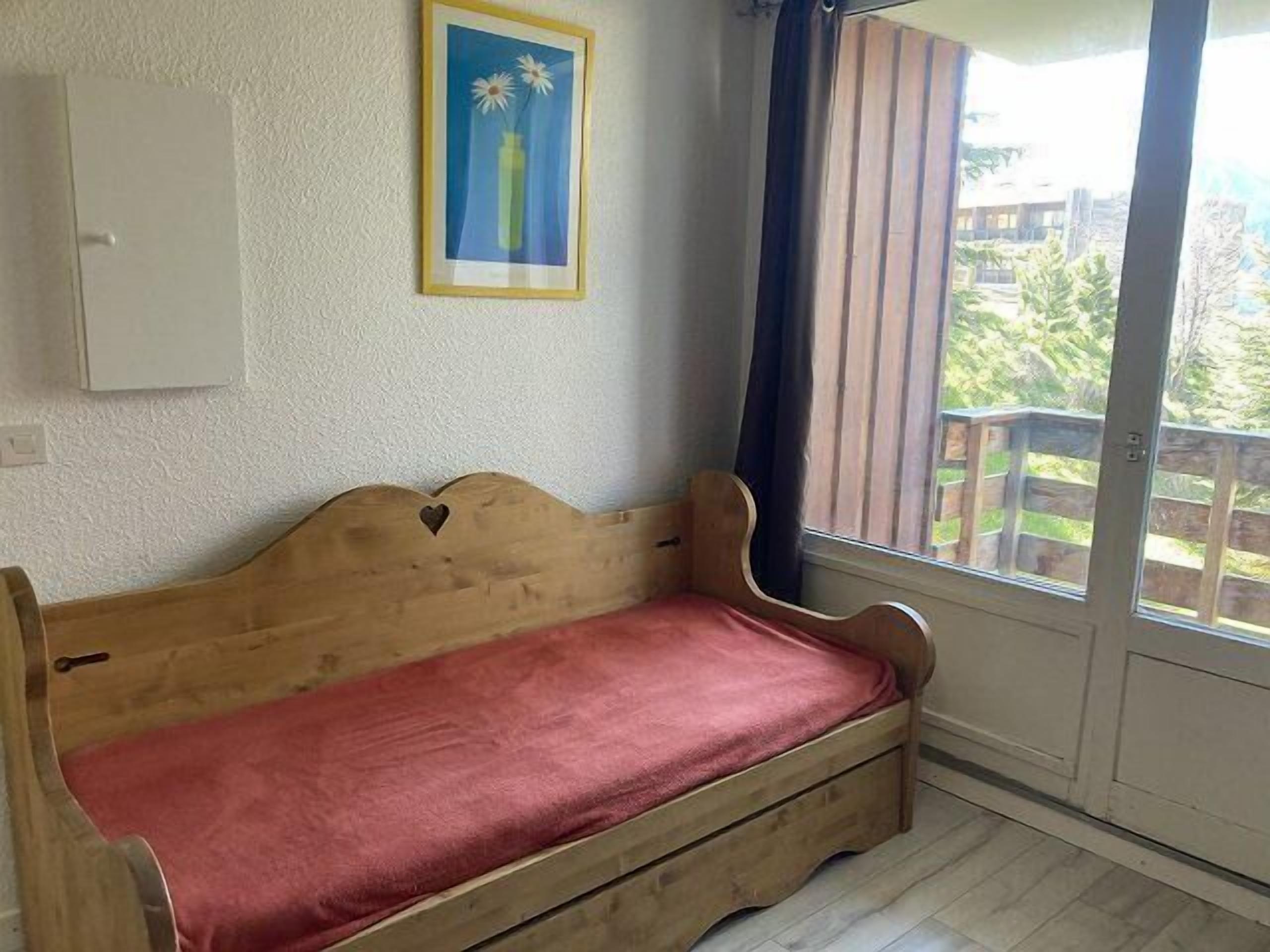 Un banco de madera con un cojín rojo, un cuadro enmarcado en la pared y vistas a un balcón con barandilla de madera.
