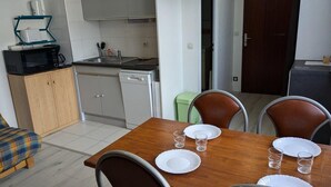 Un comedor con una mesa de madera dispuesta para cuatro, un microondas, un lavavajillas y un cubo de basura verde.