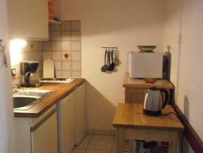 Cozinha compacta com bancada de madeira, cafeteira, chaleira e micro-ondas.