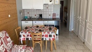 A compact kitchen with white cabinets, a dining table with chairs, and a sofa in a small living area. - 50m from ski slopes, 1st floor, terrace, tv, 40m², Orcières Merlette 1850 (Orcières)
