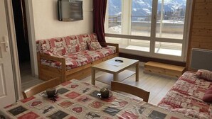 A cozy room with a sofa, a table, and a bed, featuring a mountain view through large windows. - 50m from ski slopes, 1st floor, terrace, tv, 40m², Orcières Merlette 1850 (Orcières)