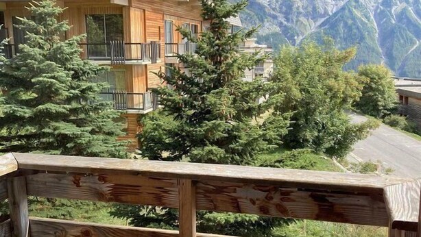 A wooden balcony with a view of a mountain range and a building with balconies.