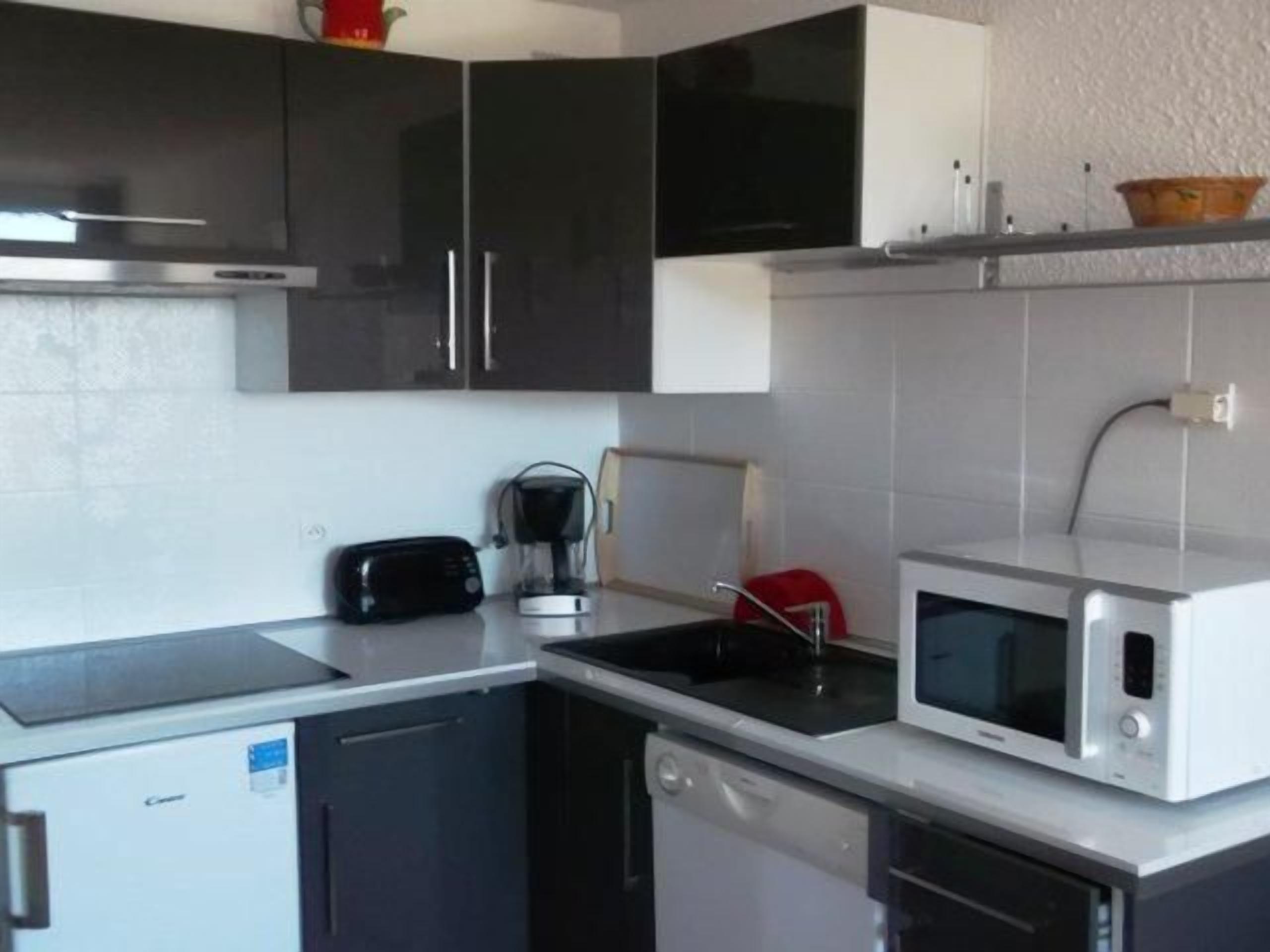 A compact kitchen with a dishwasher, a toaster, a coffee maker, and a microwave.