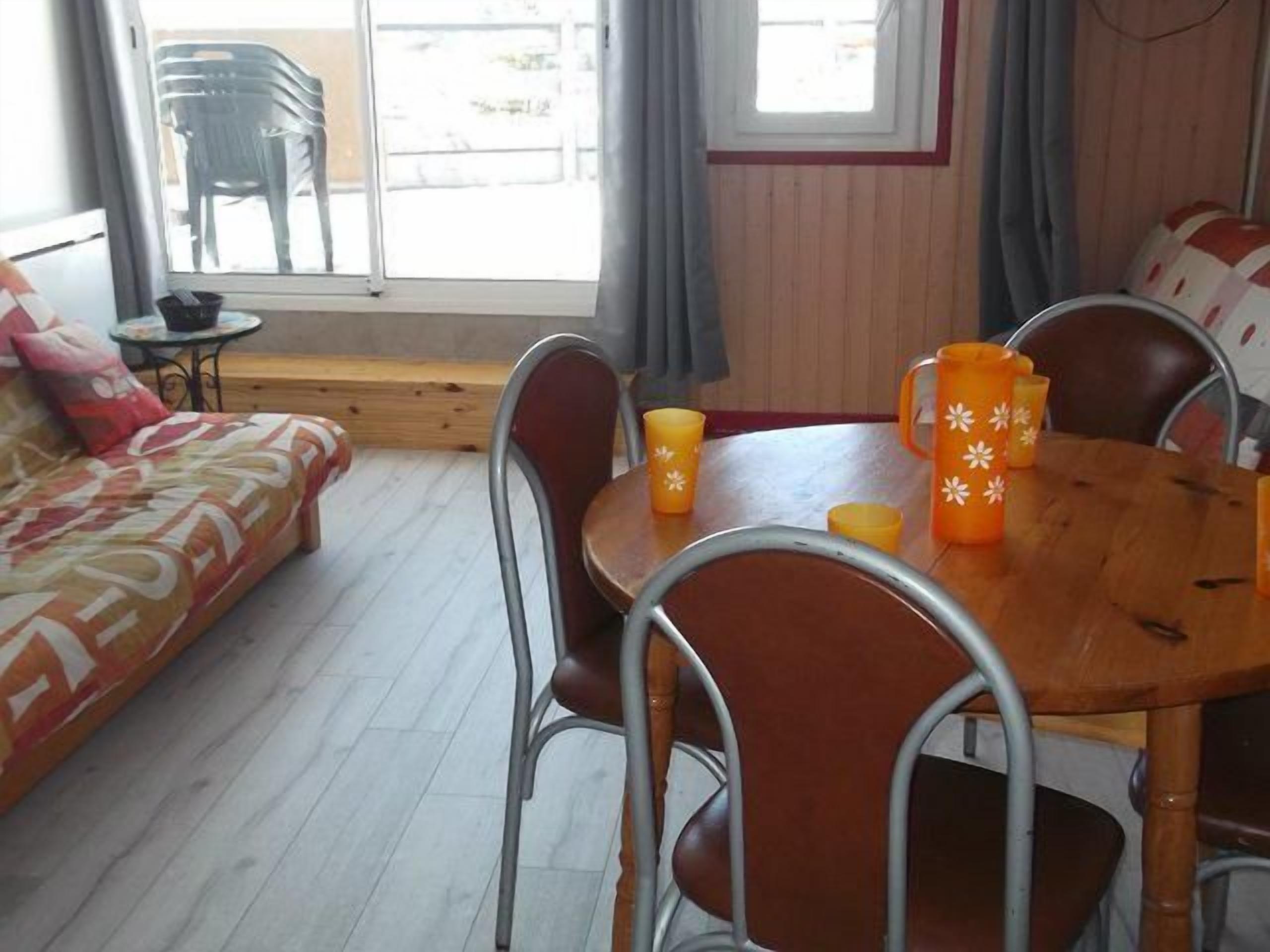 A cozy room with a wooden floor, a sofa, a dining table with chairs, and a window with curtains.