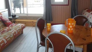 A cozy room with a wooden floor, a sofa, a dining table with chairs, and a window with curtains.