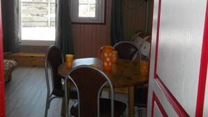 A dining area with a wooden table and metal chairs, a window with curtains, and a television mounted on the wall.