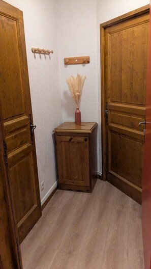 Um corredor com portas de madeira, um pequeno armário com um vaso, e uma prateleira na parede.