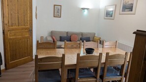 A dining area with a wooden table, chairs, and a sofa in the background.
