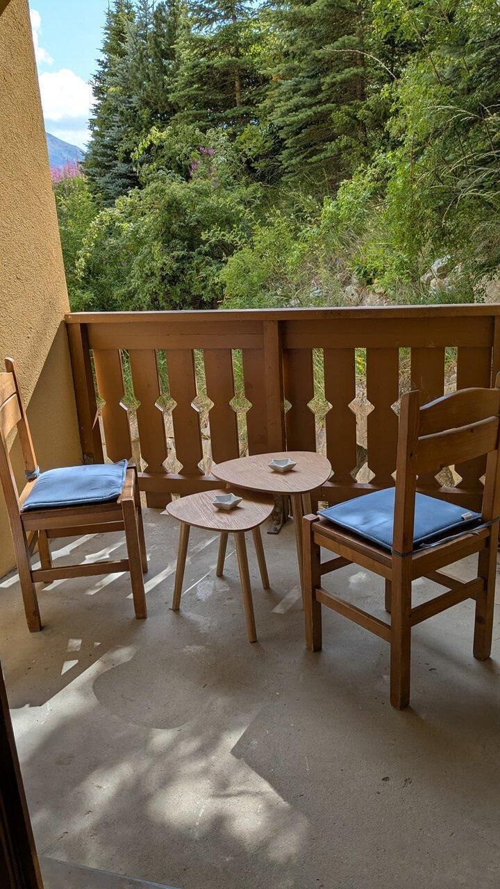A wooden outdoor seating area with two chairs and a small round table, surrounded by a wooden fence.