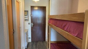 Ein schmaler Flur mit einem Holz-Etagenbett rechts, einer Tür am Ende und einer Lampe darüber.