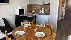 Eine kompakte Küche mit Mikrowelle, Kaffeemaschine und Geschirrspüler. Ein Esstisch mit Stühlen ist für zwei Personen gedeckt, mit Tellern und Besteck.