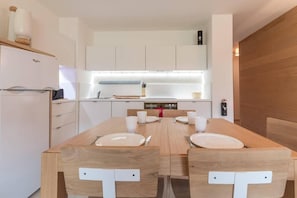A modern kitchen with white cabinetry, a wooden dining table set for two, and a built-in oven. - 190m from resort center, view valley, terrace, tv, ski locker, 65m², Montgenèvre (Montgenèvre)